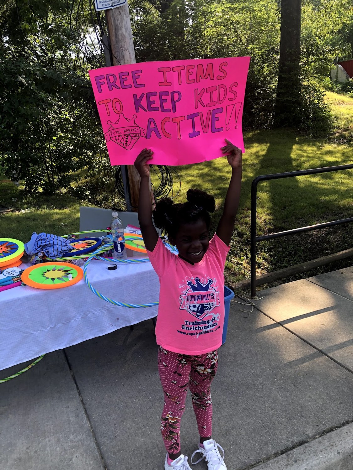 Young Royal Athlete holding a Free Items to Keep Kids Active sign at the back-to-school giveaway